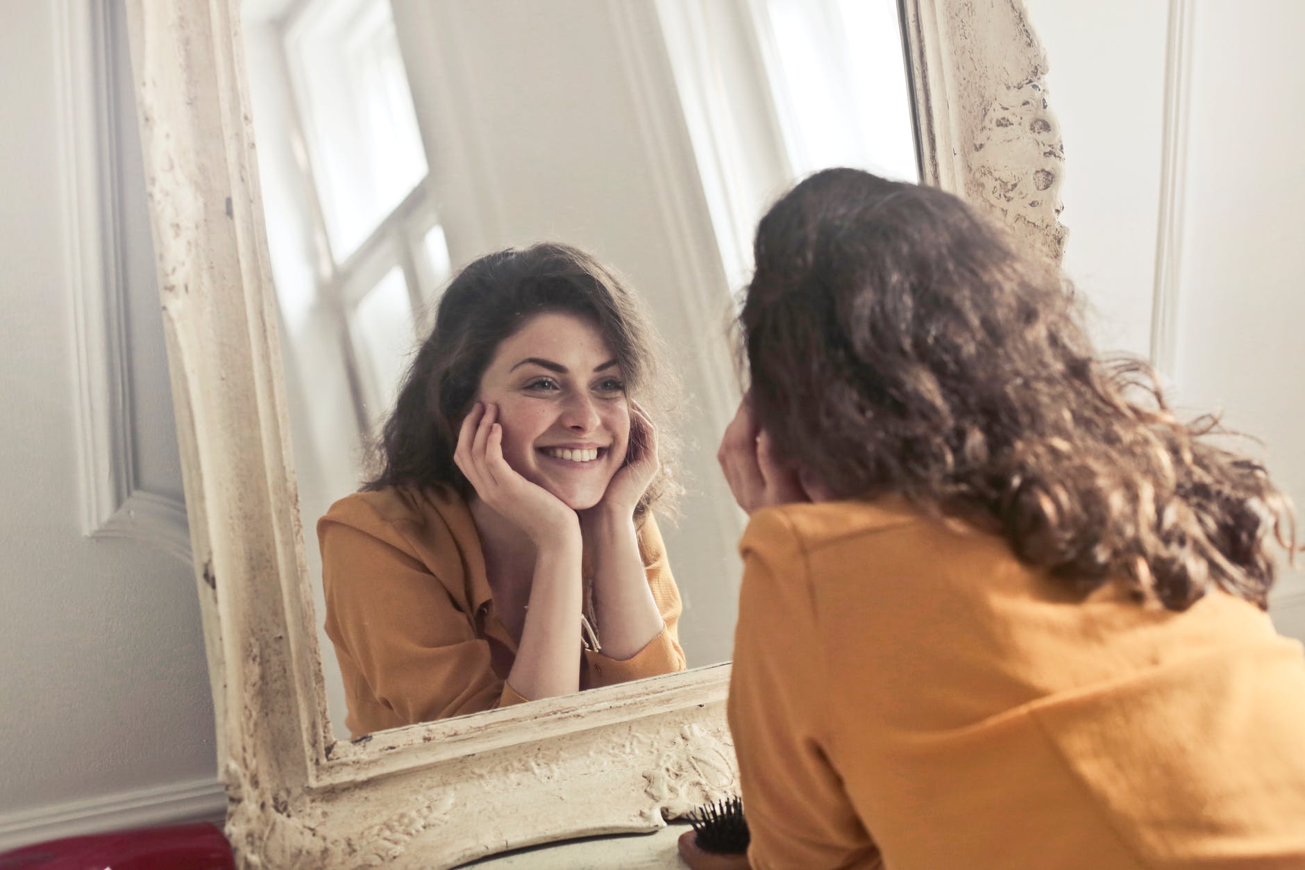 photo of woman looking at the mirror and smiling
