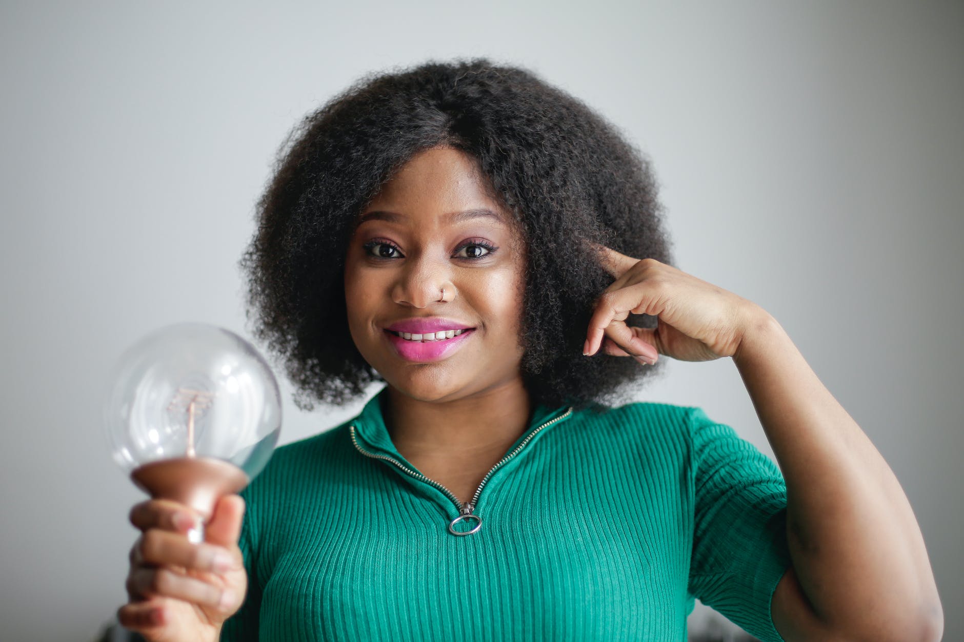 positive young african american lady holding light bulb in hand on gray background. What makes a good learner?